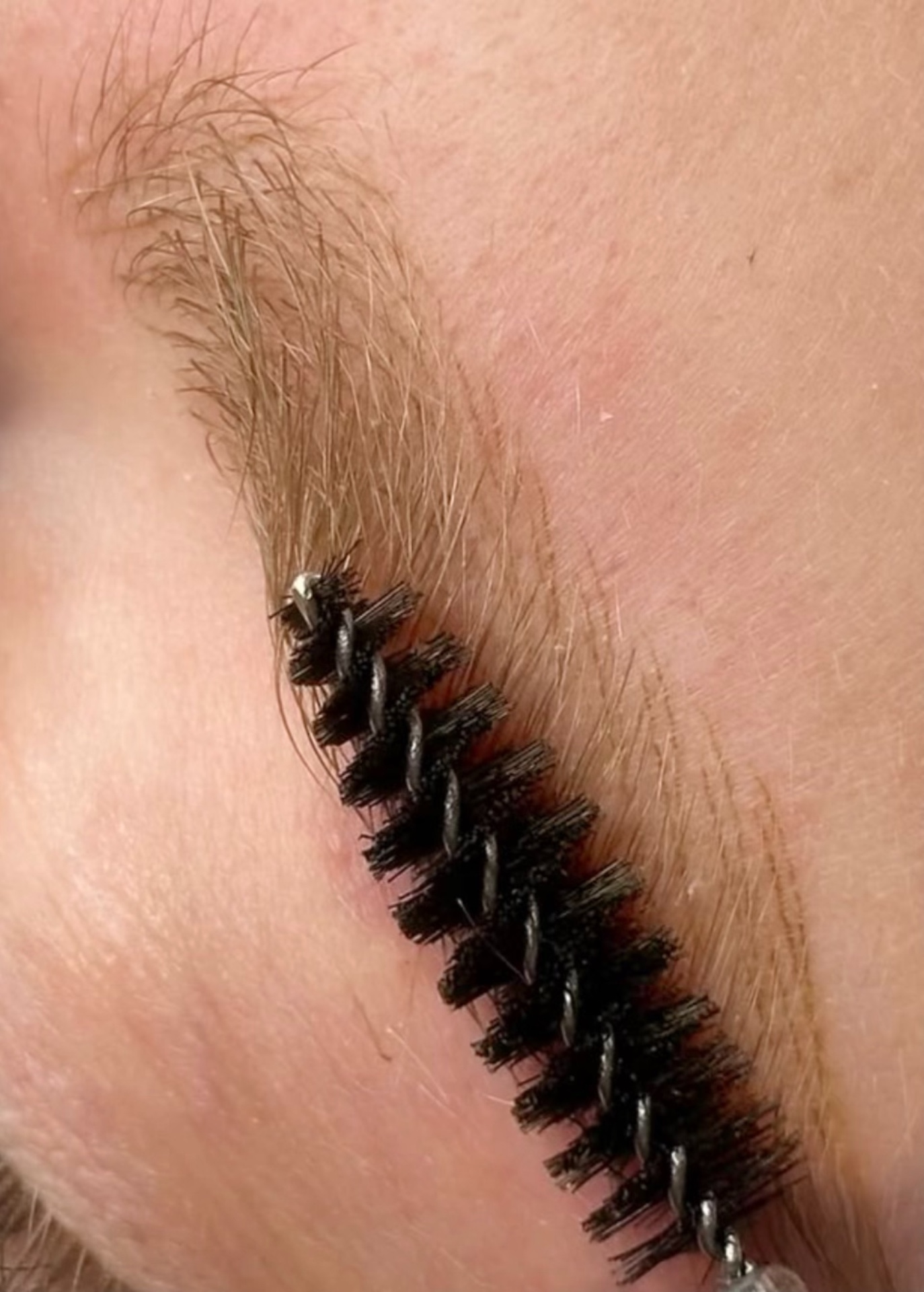 Close-up of a natural blonde eyebrow being groomed with a spoolie — soft, fair brow hair on fair skin, the typical canvas for blonde PMU at Browboutique Cascais.